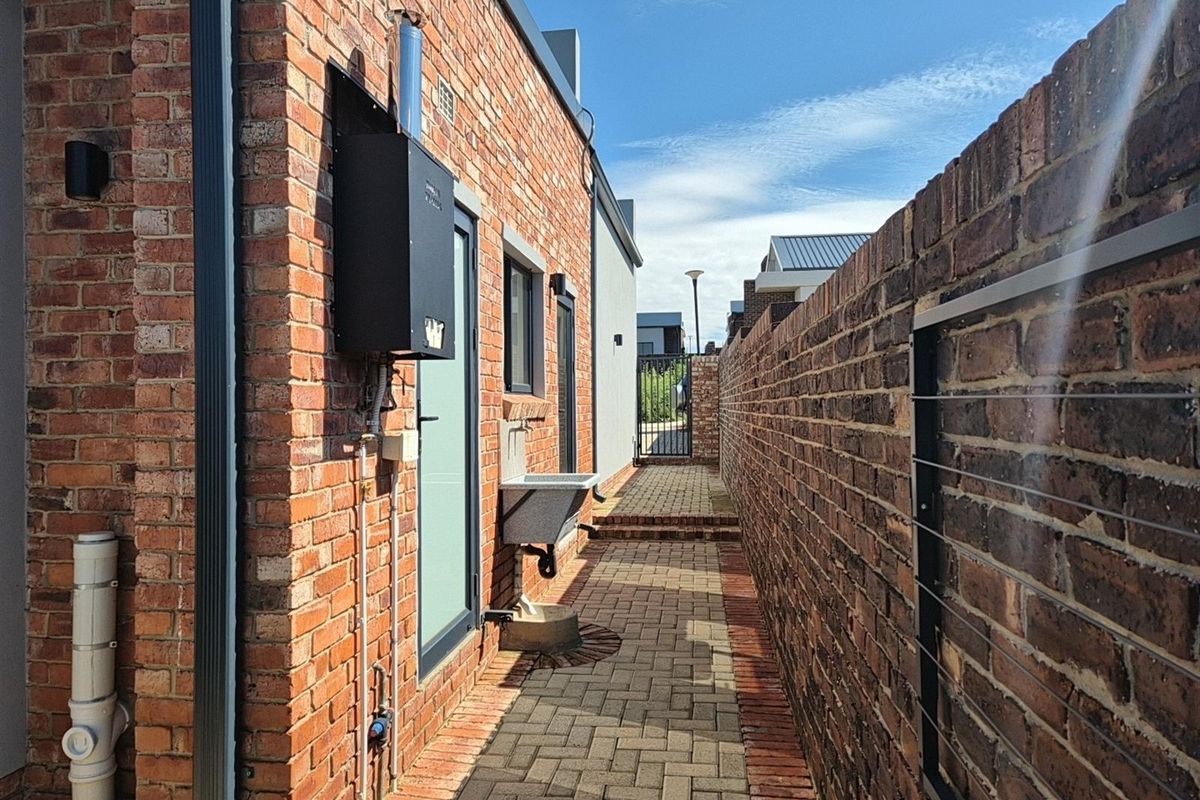 A side passage featuring brick paving, a wall-mounted utility sink, and an external gas water heater unit.
