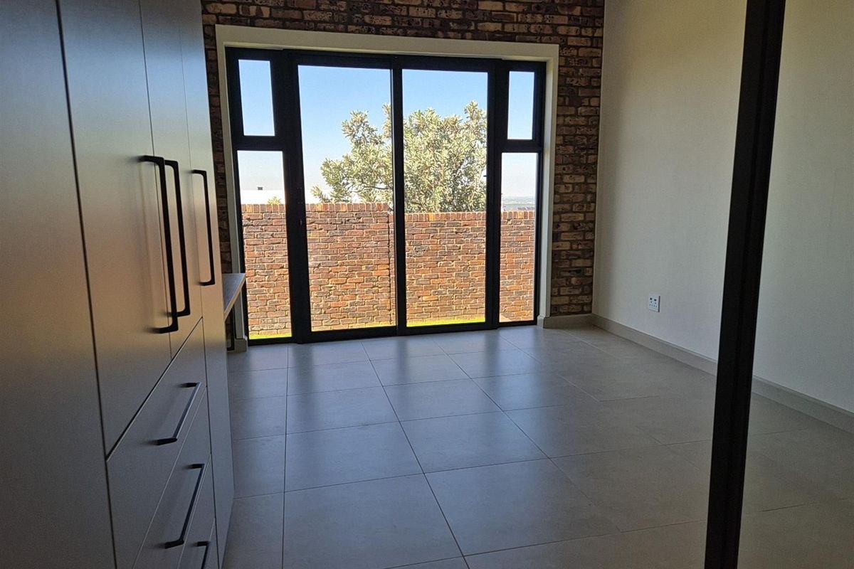 A bright bedroom featuring modern tiled flooring, built-in cabinetry, and a striking exposed brick feature wall with sliding glass doors leading outdoors.