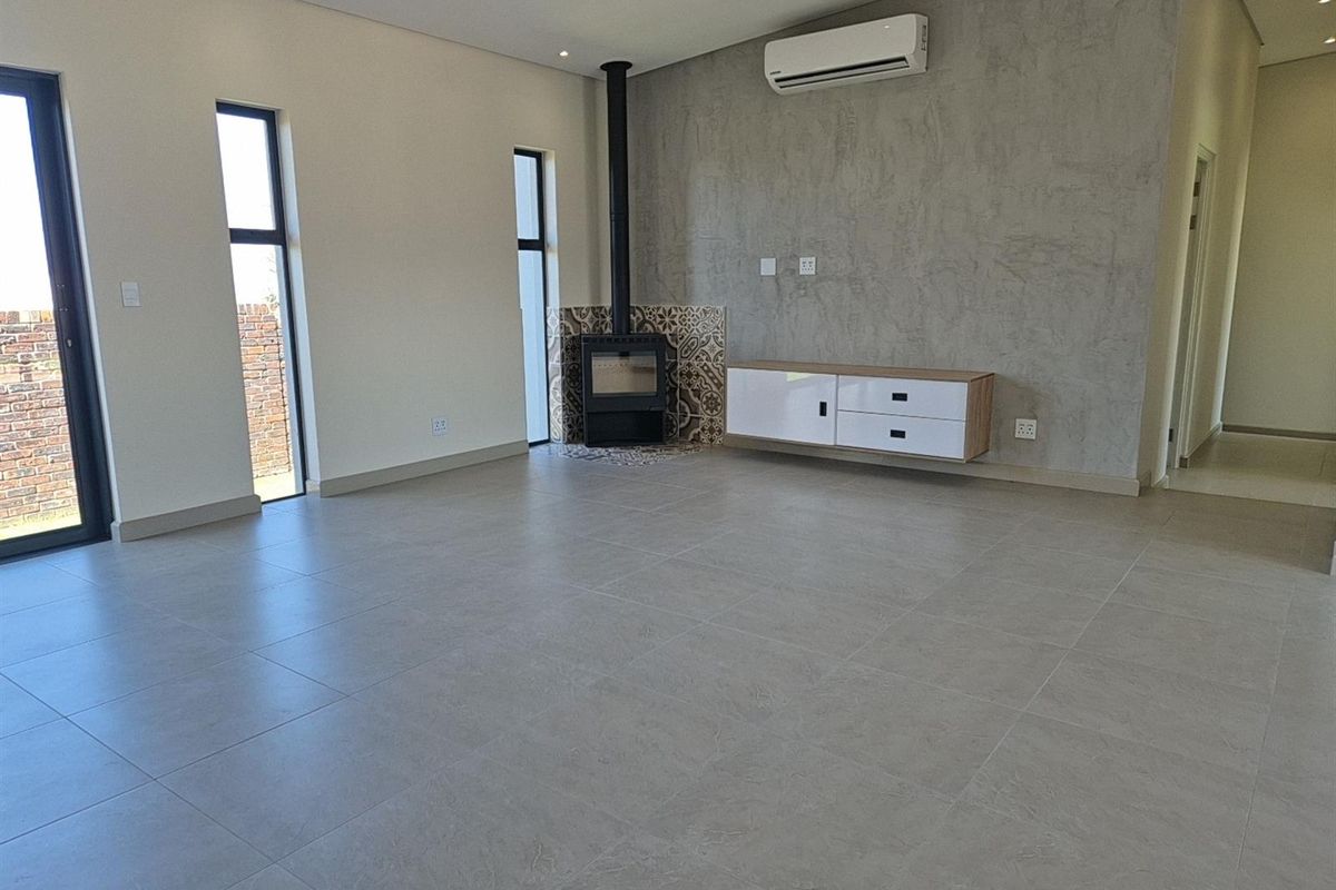 Spacious living area featuring large format floor tiles, a modern built-in fireplace with decorative tiling, and a wall-mounted air conditioning unit.