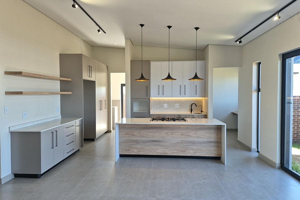 Modern open-plan kitchen featuring a central island with integrated gas hob, sleek cabinetry, stone countertops, and contemporary track lighting.