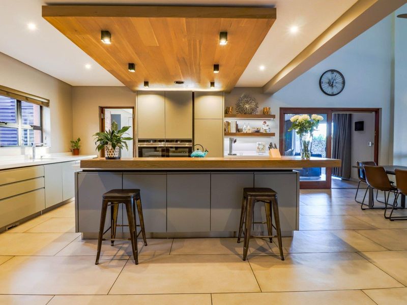 Modern open-plan kitchen featuring a large central island with timber breakfast bar, integrated cabinetry, built-in ovens, and a striking timber-clad ceiling feature with downlights.