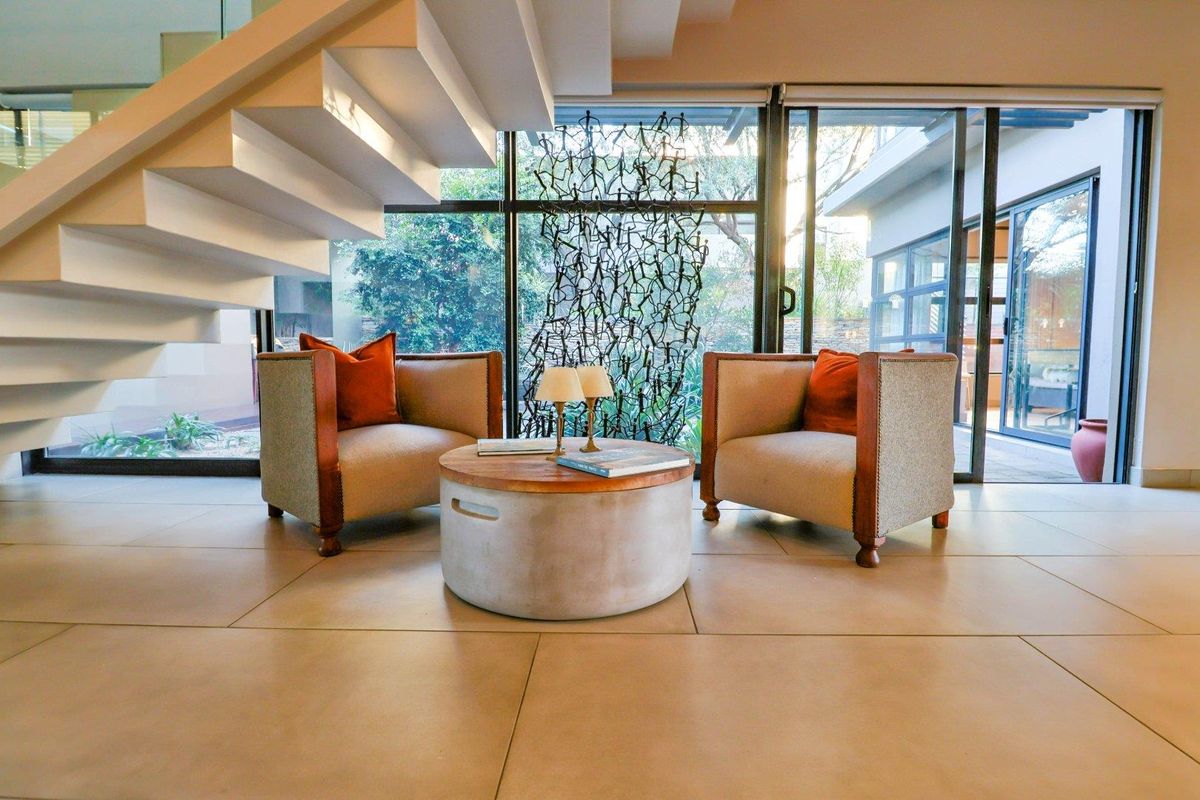 Modern living area featuring large floor-to-ceiling glass sliding doors, tiled flooring, and a contemporary floating staircase with glass balustrades.
