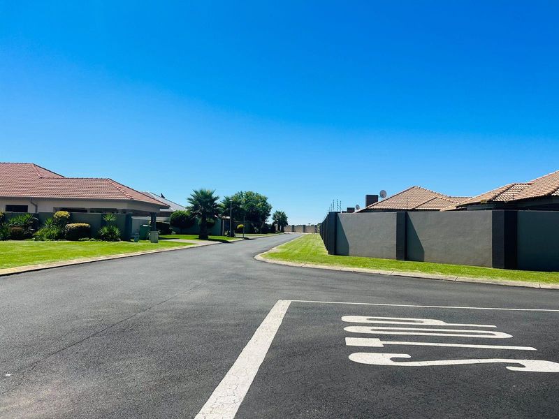 A clear street view of a well-maintained residential estate road with paved verges and boundary walls.