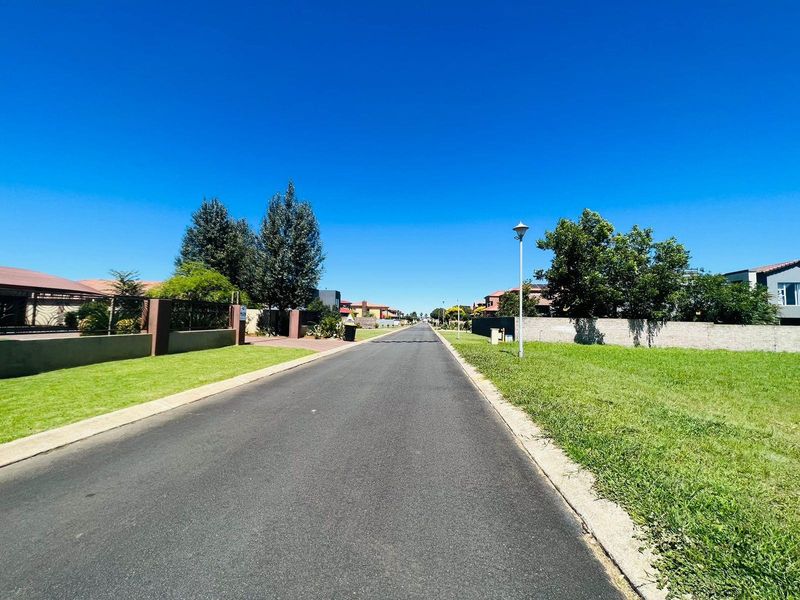 A clear view of a paved residential street within a well-maintained estate, featuring established boundary walls and street lighting.