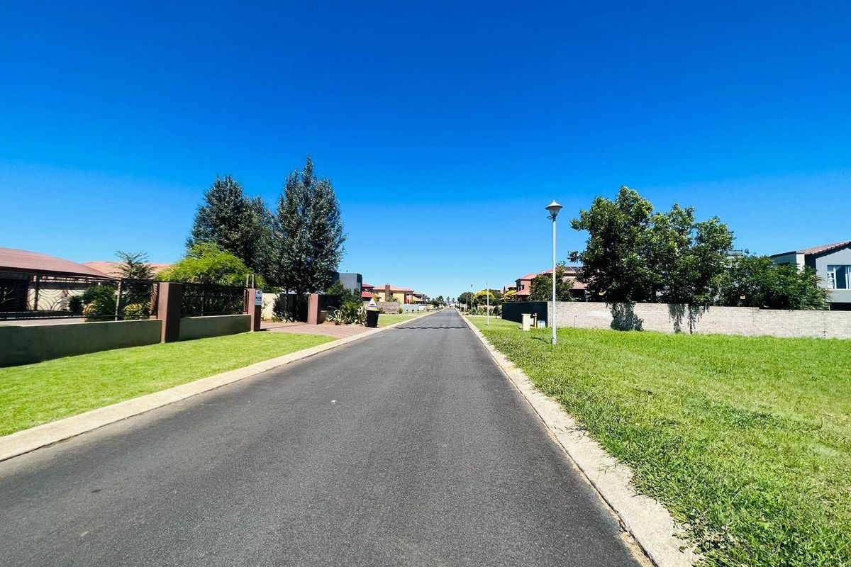 A clear view of a paved residential street within a well-maintained estate, featuring established boundary walls and street lighting.