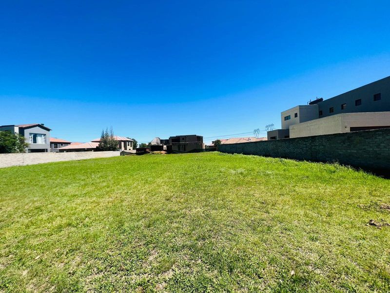 A vacant residential plot featuring a level grass lawn enclosed by boundary walls, situated within a developed neighborhood.