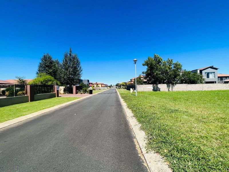 A clear street view of the residential area, featuring a paved road, established boundary walls, and street lighting in a well-maintained neighborhood.