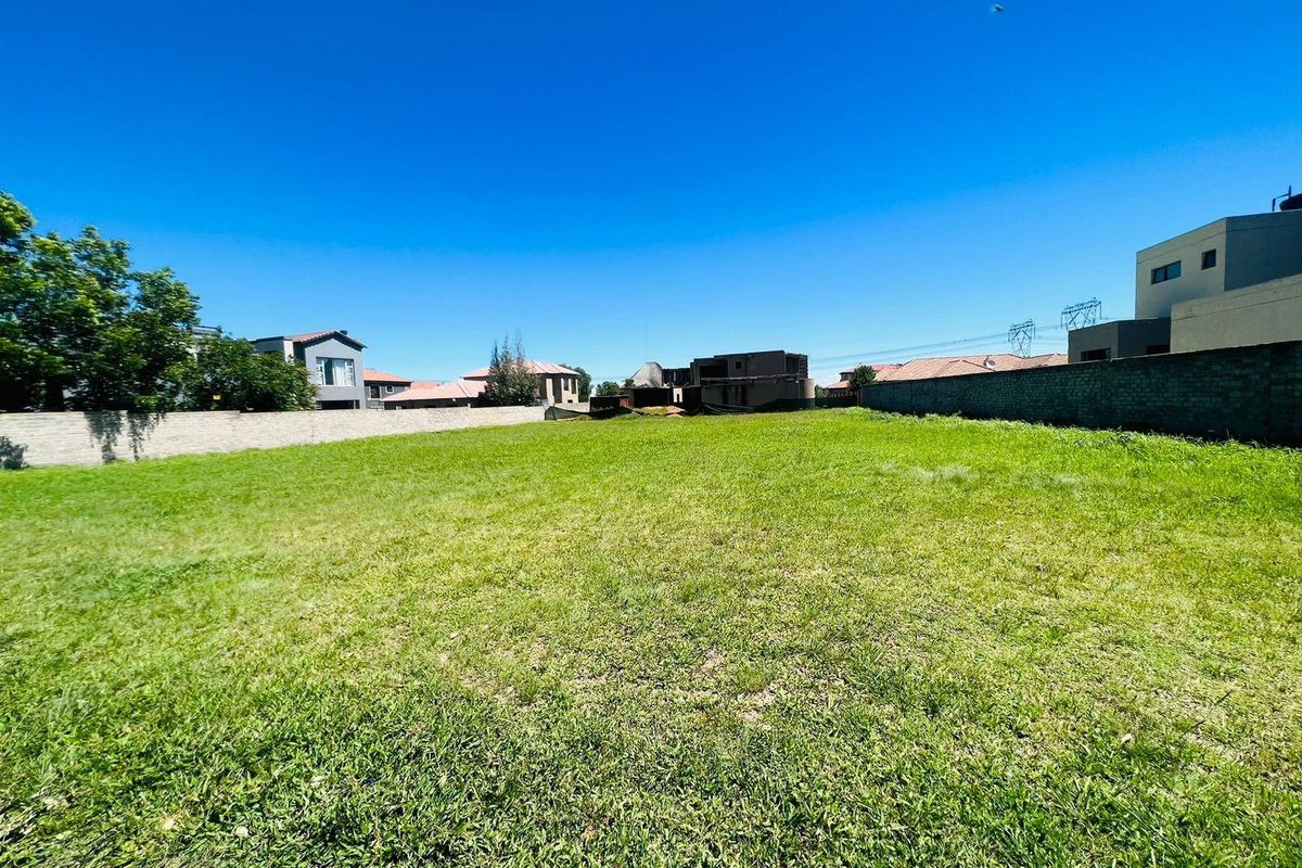 A vacant residential plot featuring a level grass lawn enclosed by perimeter boundary walls in a developed neighborhood.