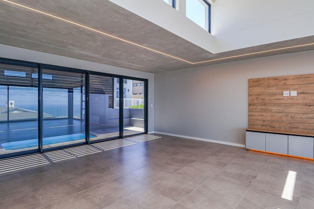 Modern open-plan living area featuring large sliding glass doors, recessed LED lighting, tiled flooring, and a built-in media console with wood-look paneling.