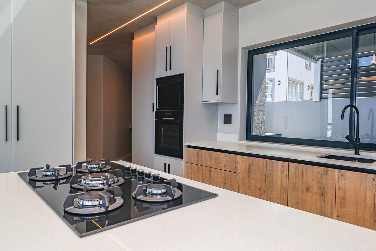 Modern kitchen featuring a central island with a built-in gas hob, sleek cabinetry, integrated oven, and a contemporary sink with matte black fixtures.