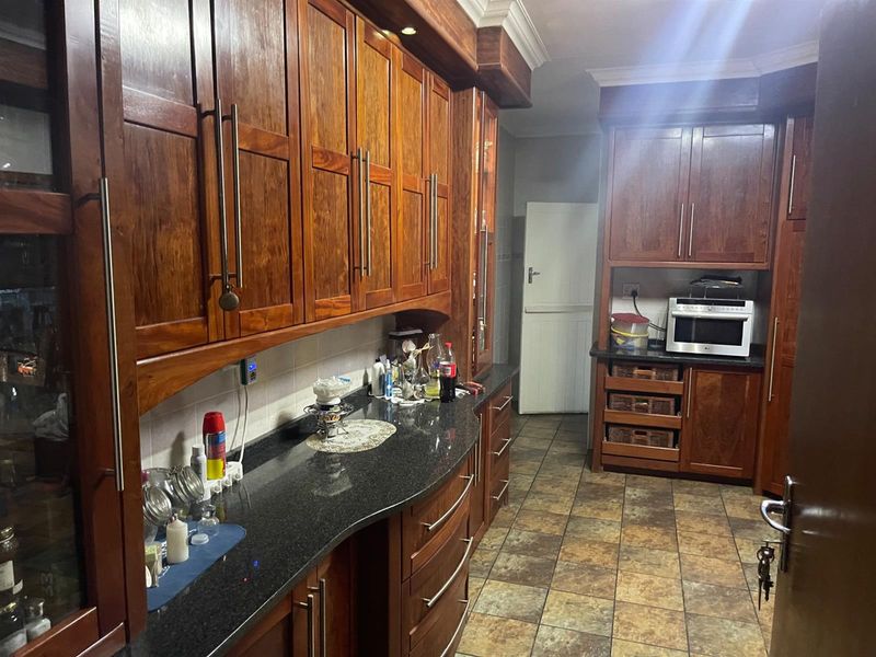 A traditional kitchen featuring rich wooden cabinetry, dark granite countertops, and tiled flooring, offering ample storage and a functional layout.