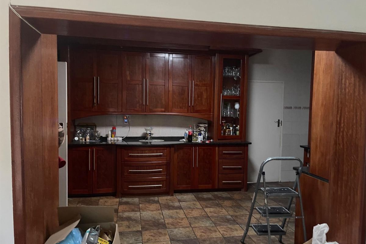 A kitchen featuring dark wood cabinetry, granite countertops, and tiled flooring, viewed through a wooden archway.