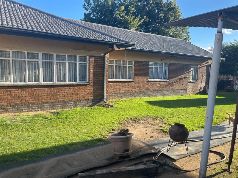 Rear view of a brick house featuring a tiled roof, multiple windows with security bars, and a spacious backyard area.