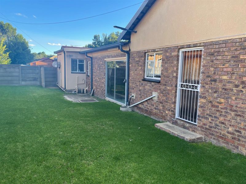 Rear view of the property featuring a brick facade, sliding glass doors, security gate, and a well-maintained lawn area.