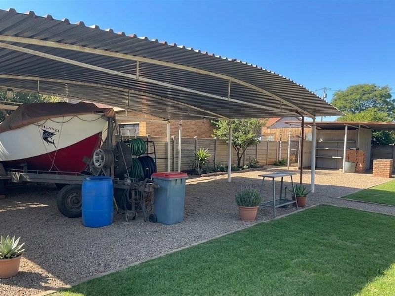 A spacious outdoor area featuring a large corrugated metal carport, gravel surfacing, and a well-maintained lawn, providing ample space for vehicle or boat storage.