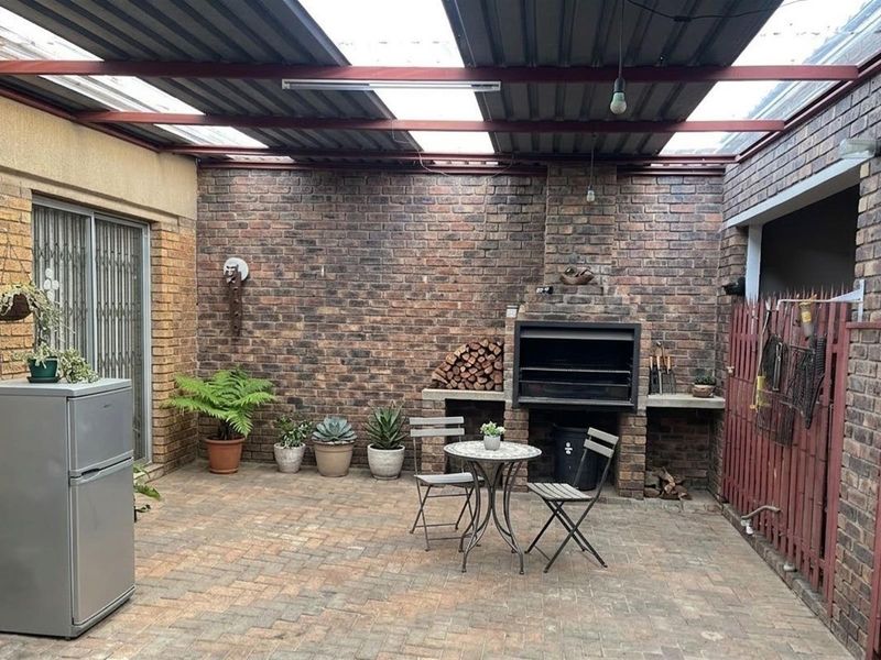Covered outdoor patio area featuring a built-in brick braai, paved flooring, and a semi-transparent roof structure, ideal for outdoor entertaining.