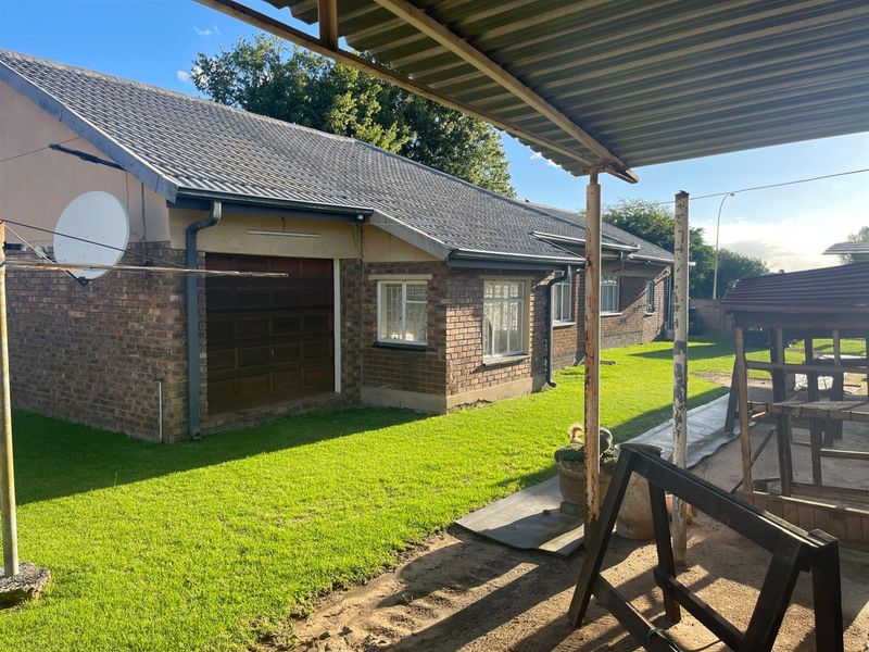 Rear view of the property featuring a brick facade, tiled roof, and a covered patio area overlooking the garden.