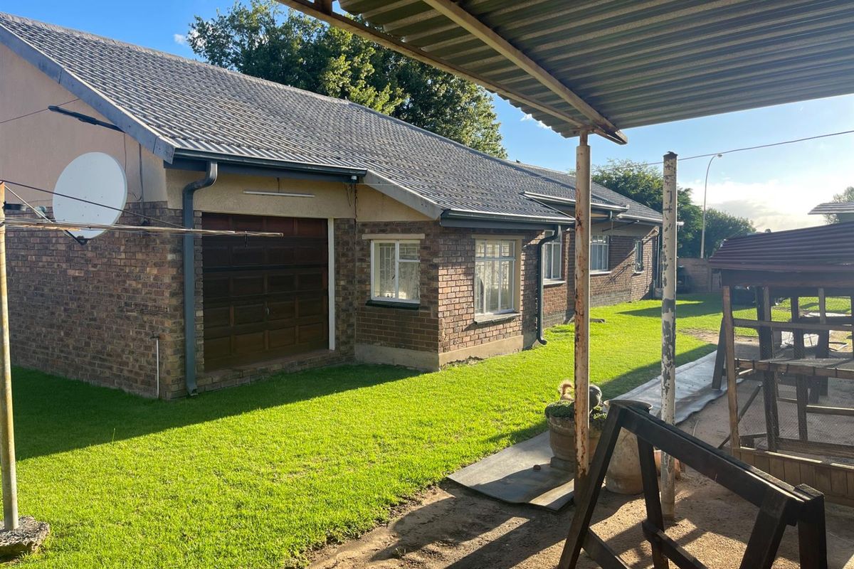 Rear view of the property featuring a brick facade, tiled roof, and a covered patio area overlooking the garden.