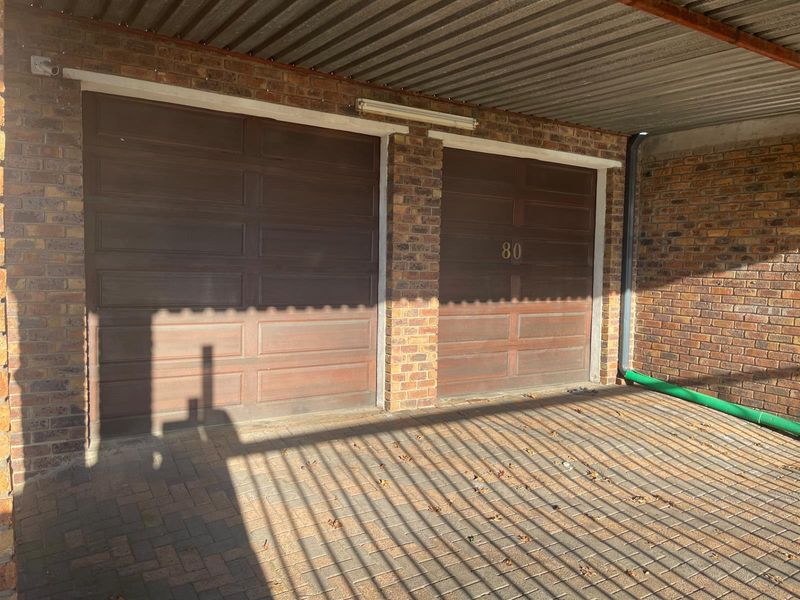 A double garage featuring brick facade construction, paved driveway, and a covered carport area.