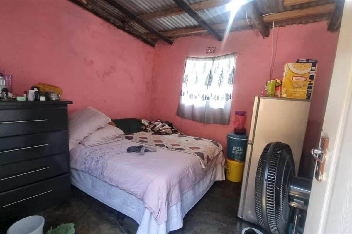A bedroom featuring exposed timber roof beams and a corrugated metal ceiling, requiring cosmetic updates to improve the overall finish and condition.