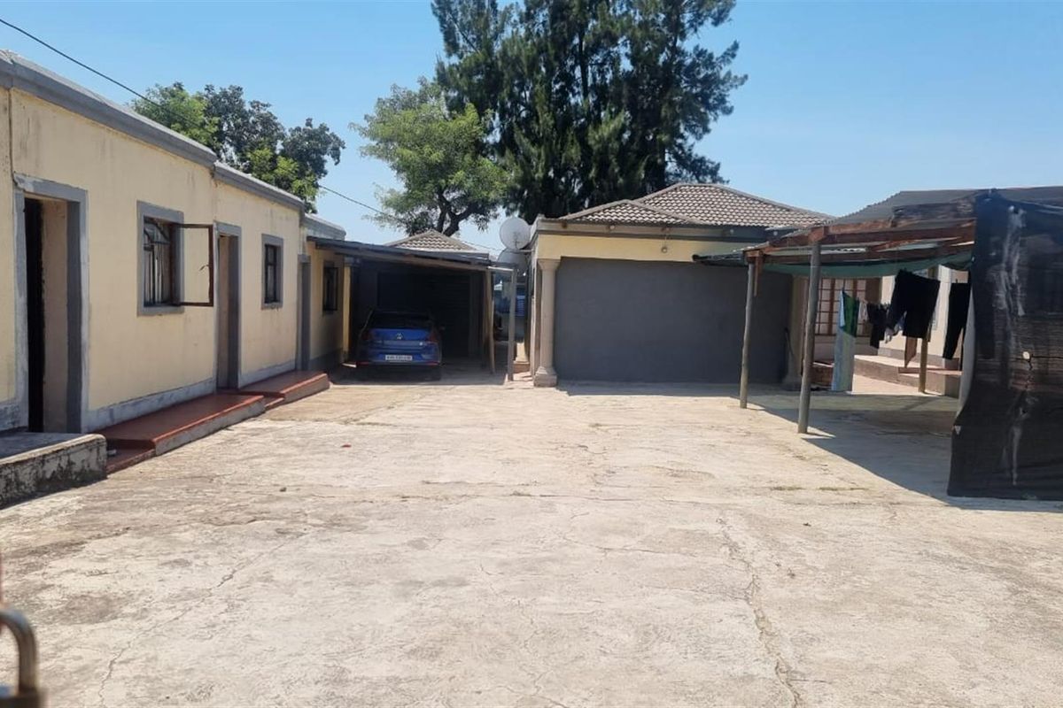 Rear exterior view of the industrial property featuring a large concrete yard, garage, and carport structure.