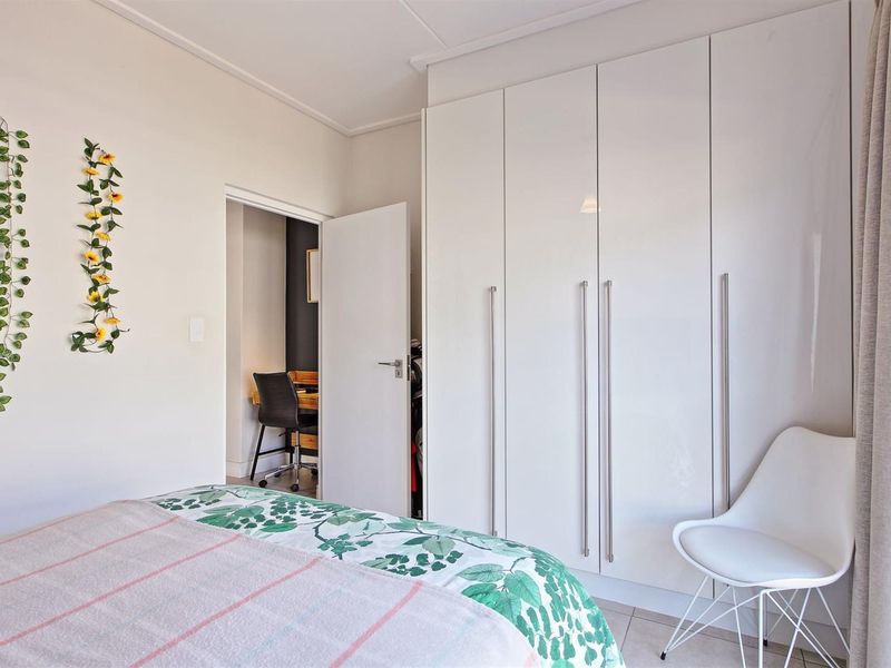 A well-maintained bedroom featuring modern white built-in cupboards and neutral tiled flooring, with an adjacent view into a small study area.