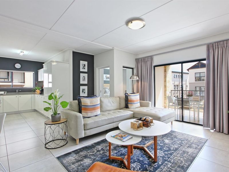 Bright open-plan living area featuring tiled floors, a modern kitchen with built-in cabinetry, and large sliding doors leading to a private balcony.