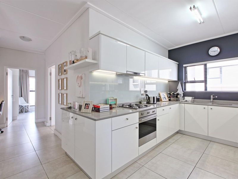 Modern kitchen featuring white high-gloss cabinetry, stone countertops, integrated gas hob, oven, and a sleek glass splashback with neutral tiled flooring.
