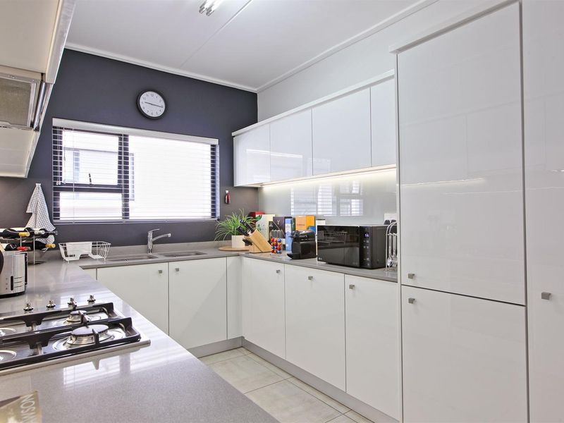 Modern kitchen featuring sleek white cabinetry, stone countertops, a gas hob, extractor fan, and integrated lighting, finished with contemporary tiled flooring.