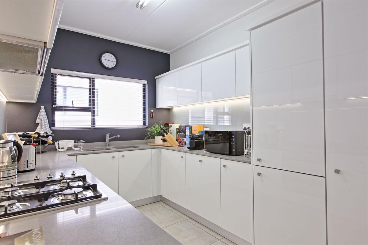 Modern kitchen featuring sleek white cabinetry, stone countertops, a gas hob, extractor fan, and integrated lighting, finished with contemporary tiled flooring.