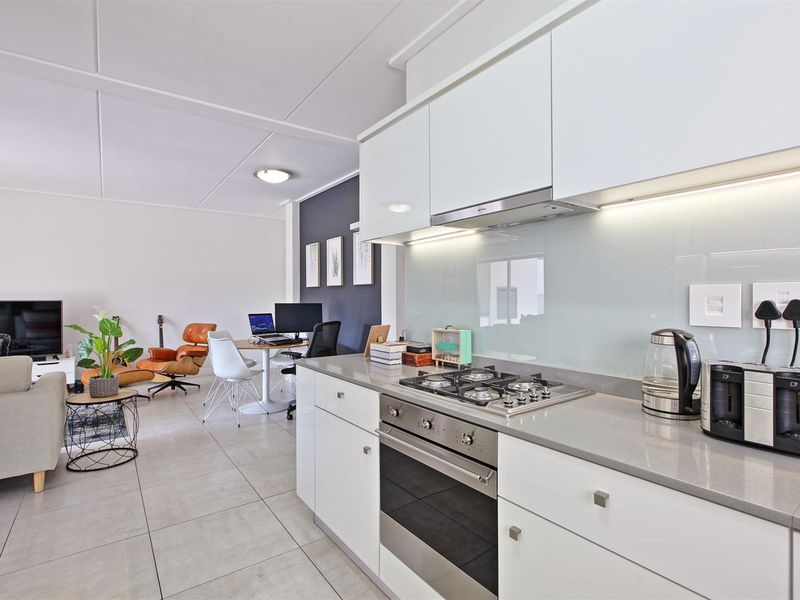 Modern open-plan living area featuring a sleek kitchen with stone countertops, gas hob, built-in oven, and glass splashback, flowing into a comfortable lounge space.