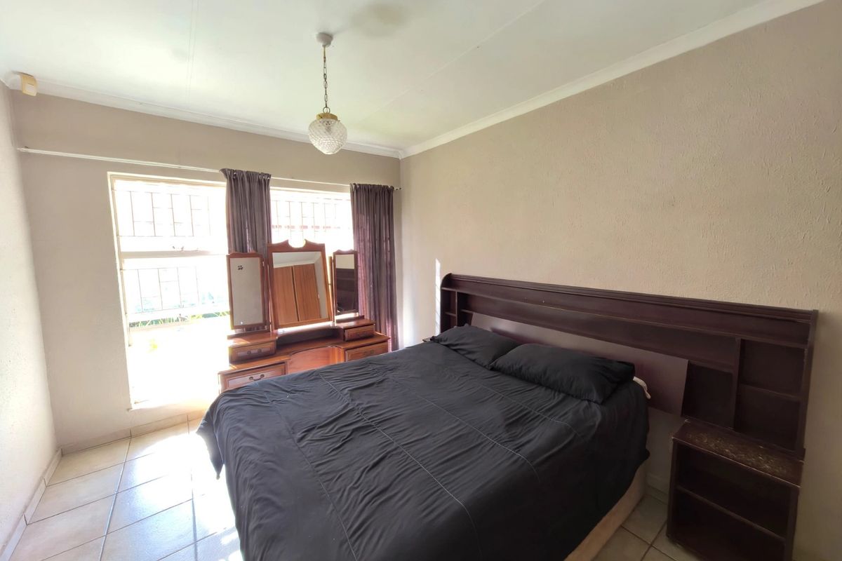 A bedroom featuring tiled flooring, coved ceilings, and large windows fitted with security bars, providing a functional and well-lit living space.