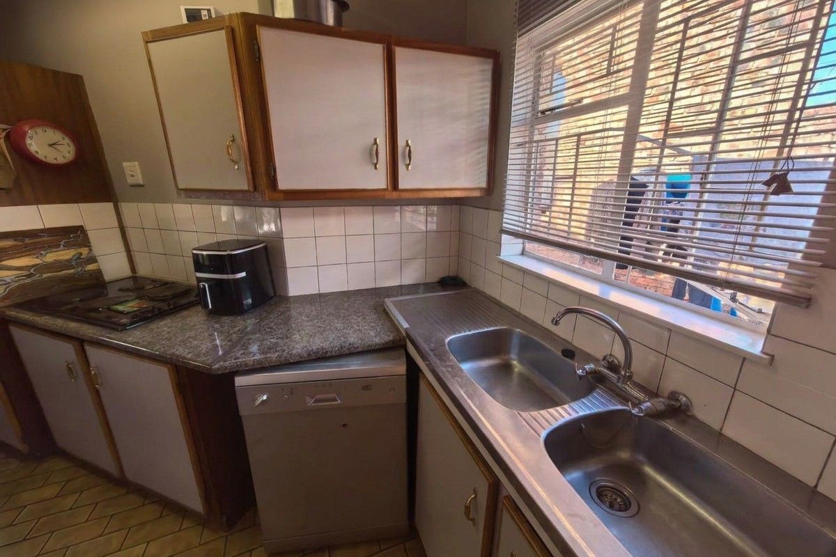 A functional kitchen featuring granite countertops, double stainless steel sink, built-in hob with extractor, and ample cabinetry, offering potential for modern cosmetic updates.
