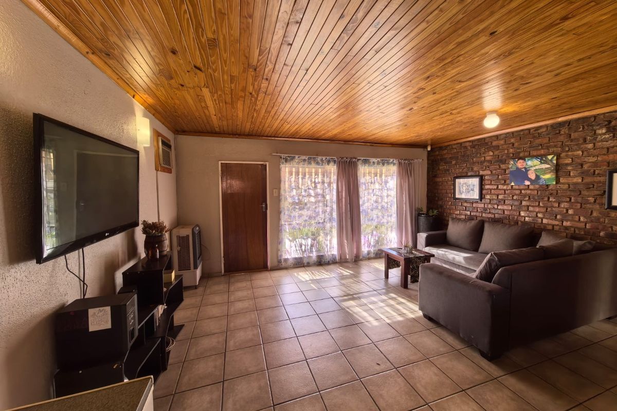 A living room featuring a rustic exposed brick wall, warm timber tongue and groove ceiling, and neutral ceramic floor tiles.