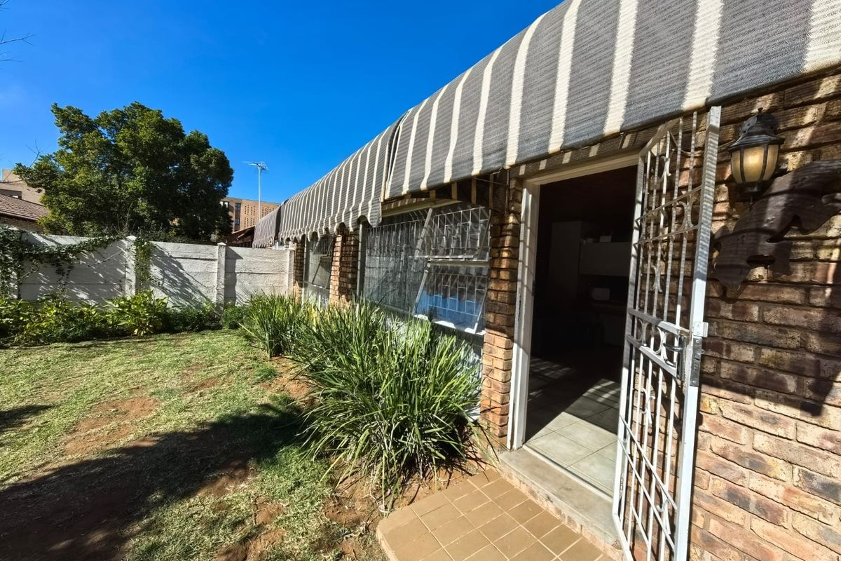 Rear exterior view of the townhouse featuring a brick facade, security gate, and a striped awning overlooking a private garden area.