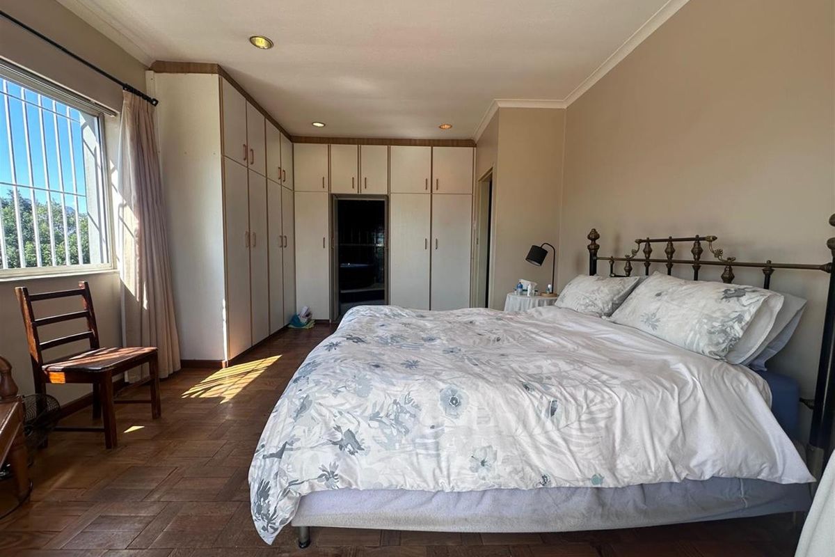 Spacious bedroom featuring extensive built-in cabinetry, parquet flooring, and large windows with security bars, offering a functional and well-lit living space.