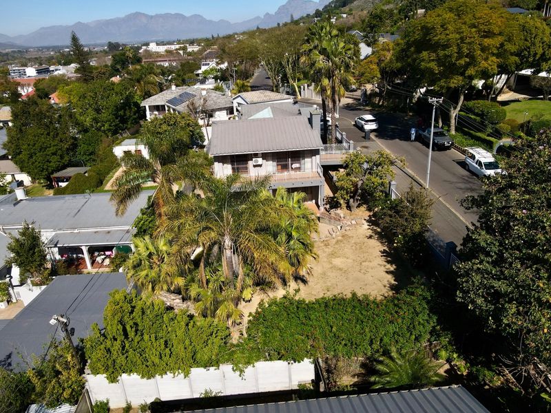 Aerial view of the property showing the main dwelling, metal roof, balcony, and surrounding garden area within a residential neighborhood.