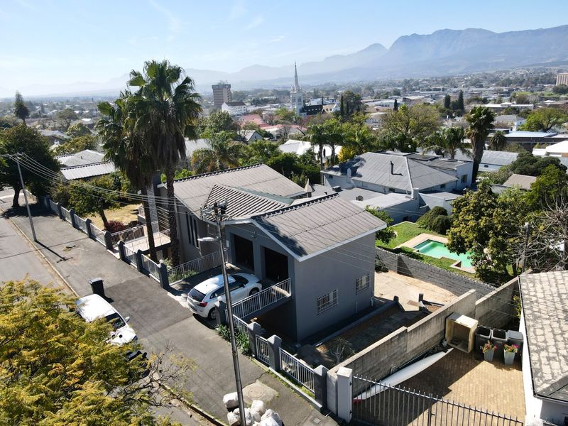 Aerial view of the property showing the main building, paved driveway, perimeter wall, and swimming pool within a residential neighborhood setting.