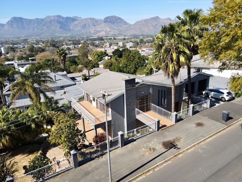 Aerial view of a modern grey house featuring a metal roof, balcony, and garage, set against a scenic mountain backdrop.