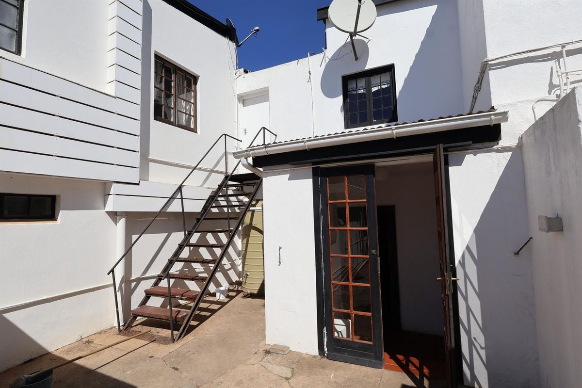 A rear exterior view of the hotel building featuring a metal staircase, white rendered walls, and a glass-paned door leading into the property.