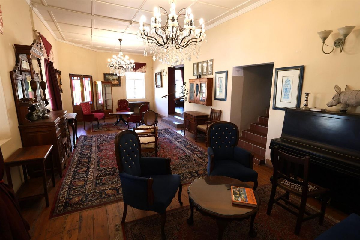 A spacious hotel lounge area featuring traditional timber flooring, ornate chandeliers, and a classic interior layout with access to adjacent rooms.