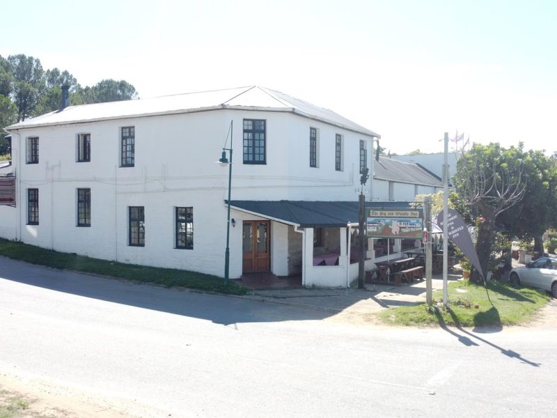 Exterior view of a two-story hotel building featuring a white facade, metal roof, and a covered ground-floor patio area.