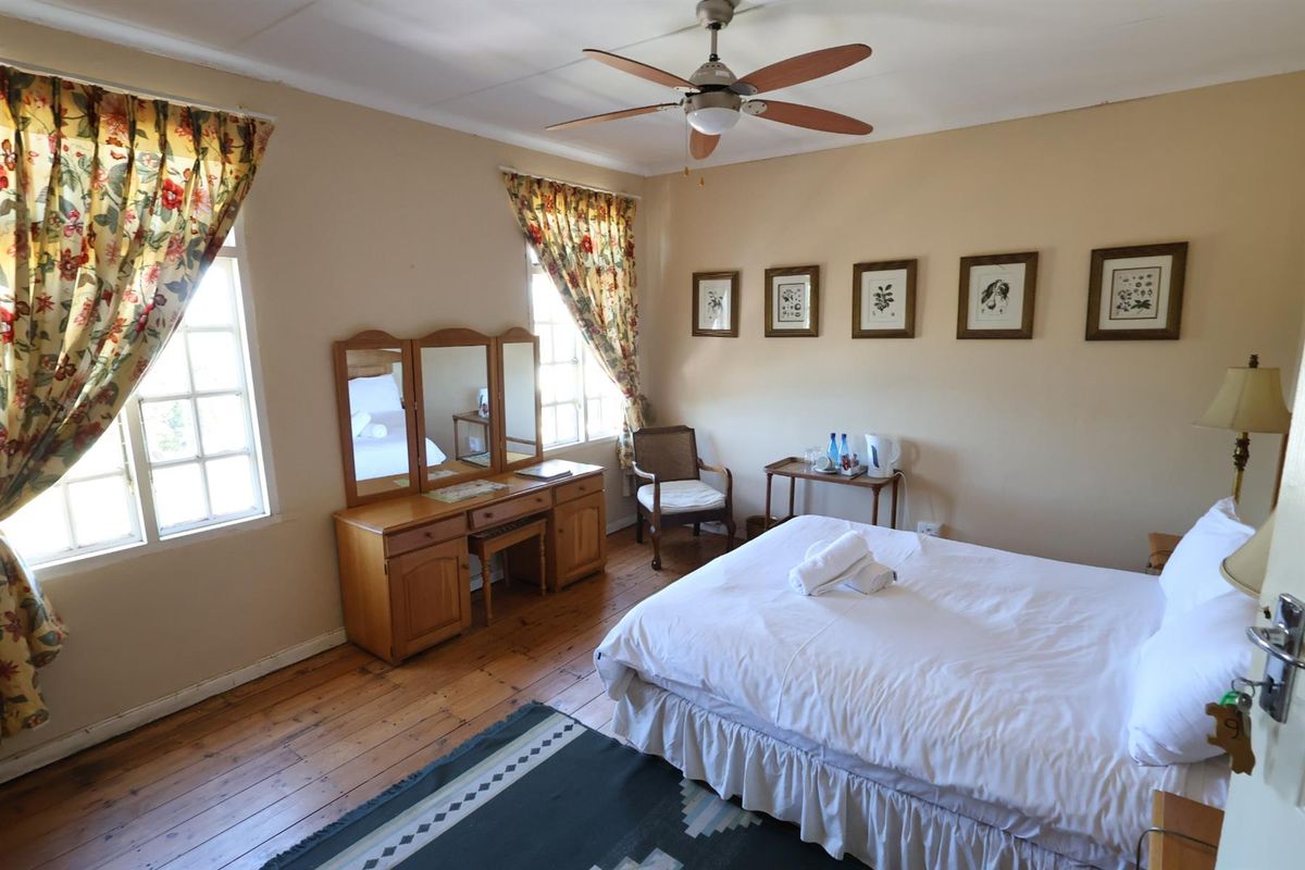 A classic hotel bedroom featuring timber flooring, a ceiling fan, and large windows that provide natural light.