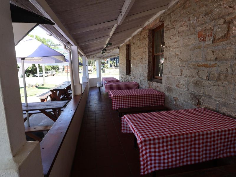 A covered outdoor patio area featuring rustic stone walling, tiled flooring, and a timber-framed roof structure, ideal for alfresco dining.