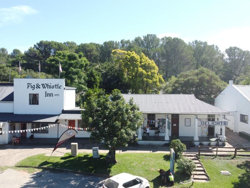 Aerial view of the Pig & Whistle Inn, showcasing the historic building complex with its white facade, corrugated metal roofing, and surrounding landscaped grounds.