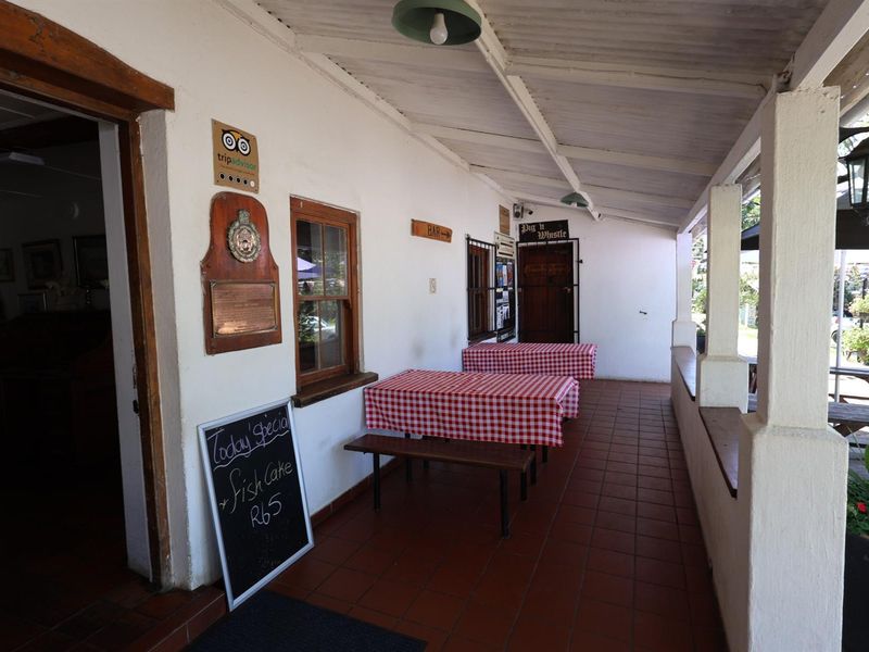 A covered outdoor patio area featuring tiled flooring, white rendered walls, and structural support pillars, providing an inviting space for outdoor dining.