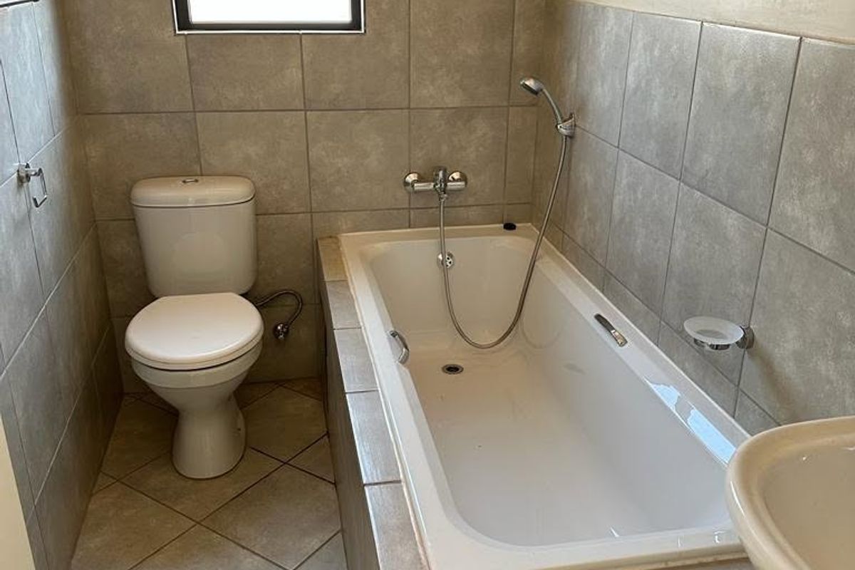 A functional bathroom featuring a built-in bathtub with shower attachment, a standard toilet, and neutral tiled finishes throughout.