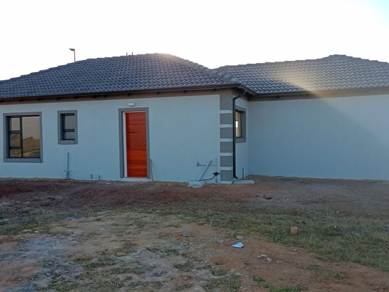 Rear view of a modern single-story house featuring a tiled roof, painted exterior walls, and aluminium window frames, set on an unlandscaped plot.