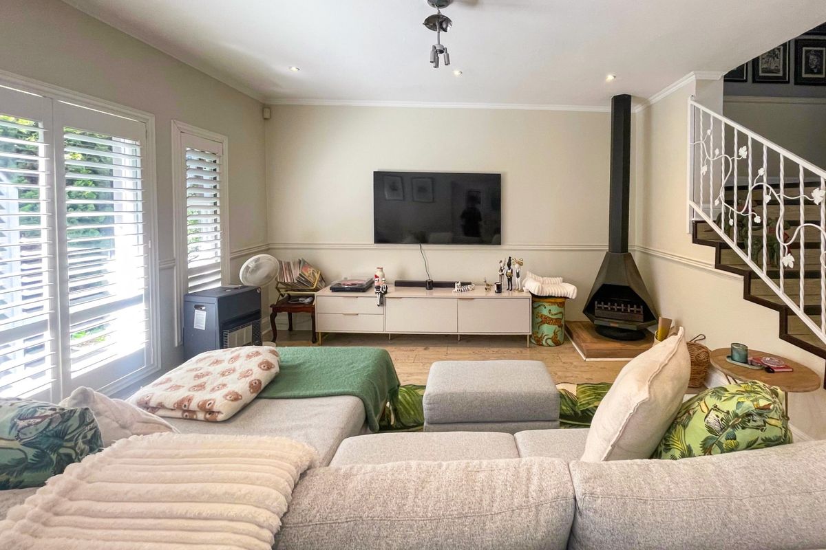 A comfortable living room featuring a modern fireplace, elegant plantation shutters, and a staircase with a decorative wrought iron balustrade.