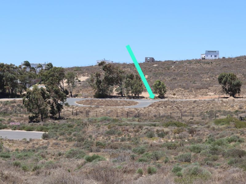 An elevated view of a vacant residential plot featuring native vegetation, perimeter fencing, and access to a paved road in a quiet neighborhood.